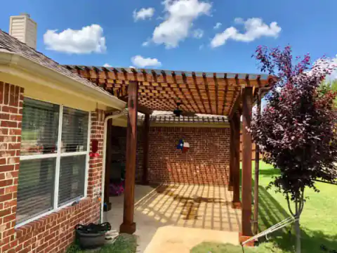 Cedar pergola shades a brick home's concrete walkway.