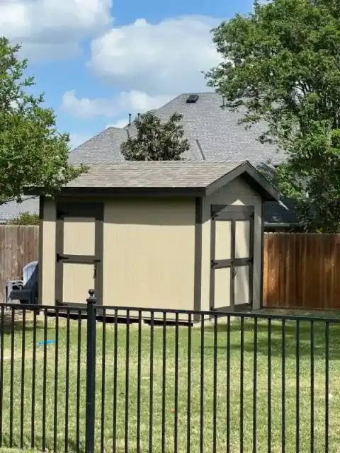 Black-framed fence encloses a small backyard shed.