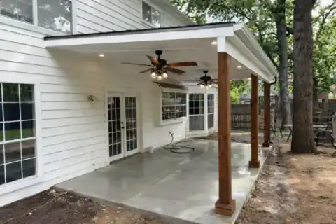 Covered patio addition shades the rear of a white-sided home.
