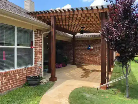 Cedar pergola adds shade along a brick home's patio.