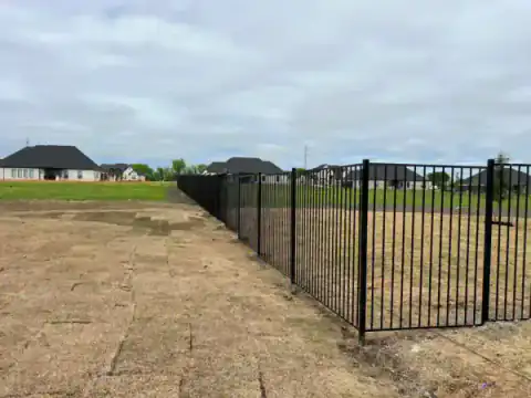 Black metal fence encloses a wide open residential lot.