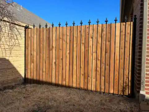 Cedar privacy fence with decorative finials meets a brick wall.