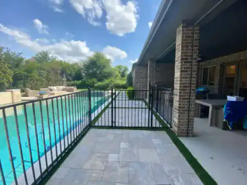 Black metal pool gate follows a concrete patio edge.