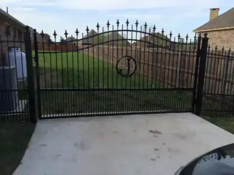 Black metal driveway gate with an arched top at a brick home.