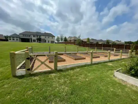 Wood-framed animal enclosure with gates fills a grassy field.