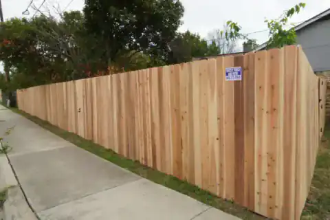 Cedar fence with a Grizzly Fence and Patio sign lines a sidewalk.