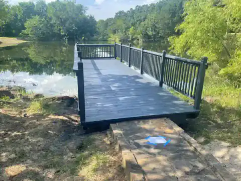 Black-railed footbridge crosses a pond in a wooded setting.