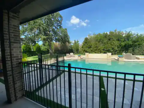 Black metal pool railing borders a backyard swimming pool.