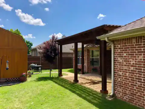 Cedar pergola shades a brick home's rear patio.