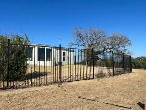 Black metal perimeter fence encloses an open North Texas lot.