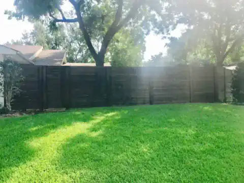 Dark-stained cedar fence spans a bright green backyard.