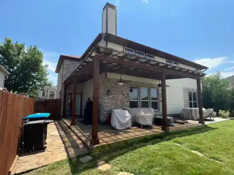 Cedar pergola frames a brick home's backyard patio.
