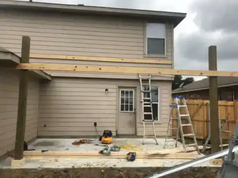 Patio cover and concrete work continue behind a white-sided home.